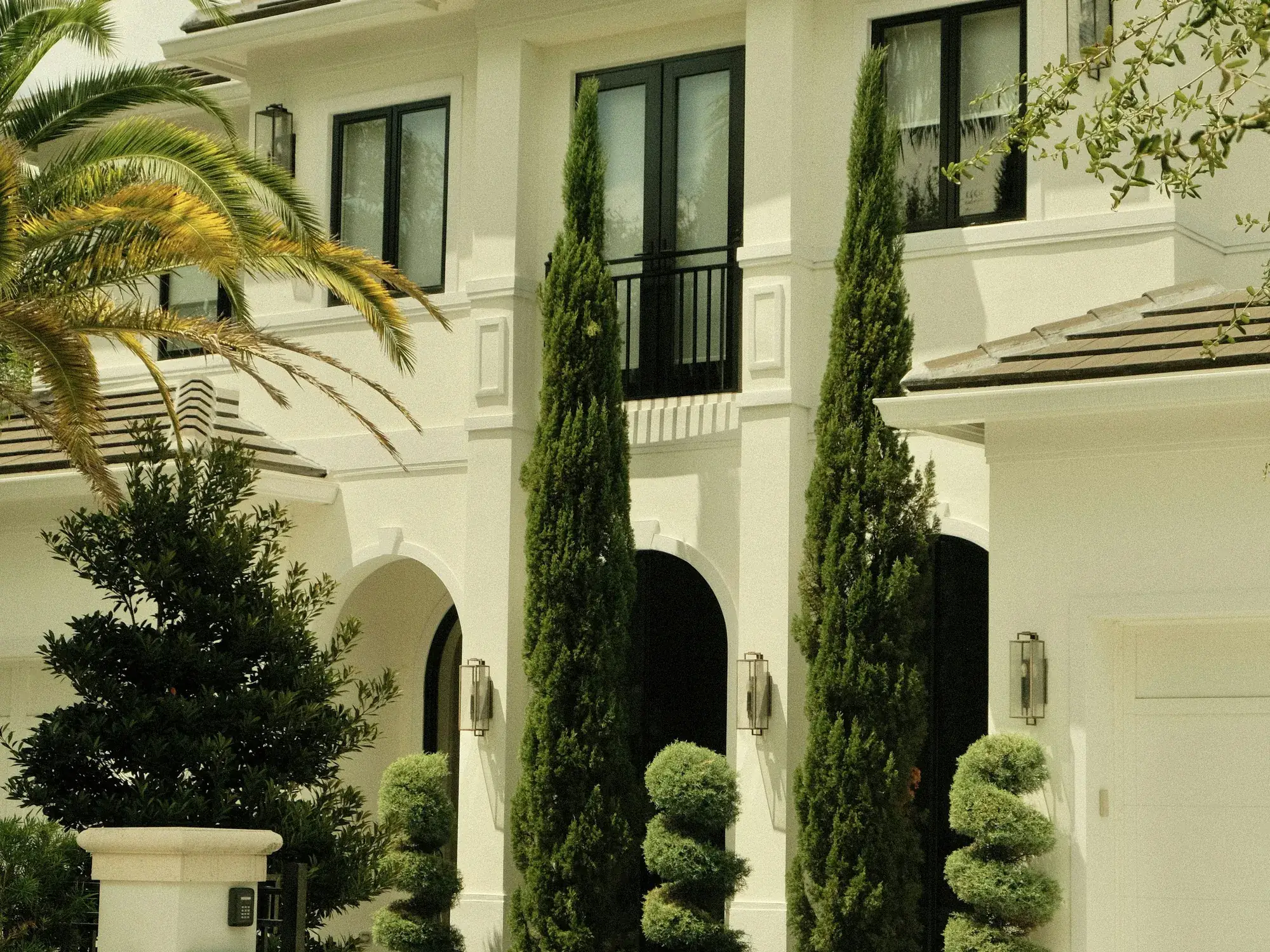 Modern French-style villa facade with tall black-framed French windows, wrought-iron balcony and arched entries